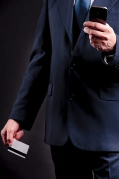 an old businessman with a credit card and a mobile hphone making purchases online  DARK BACKGROUND