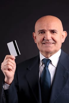 an old businessman with a credit card and a mobile hphone making purchases online  DARK BACKGROUND