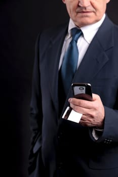 an old businessman with a credit card and a mobile hphone making purchases online  DARK BACKGROUND