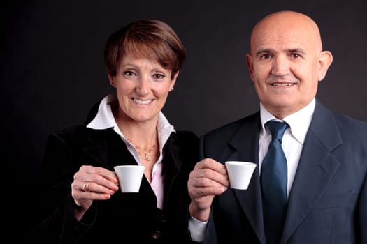 a smiling elderly couple holding up two cups of italian espreso coffee and smiling each other