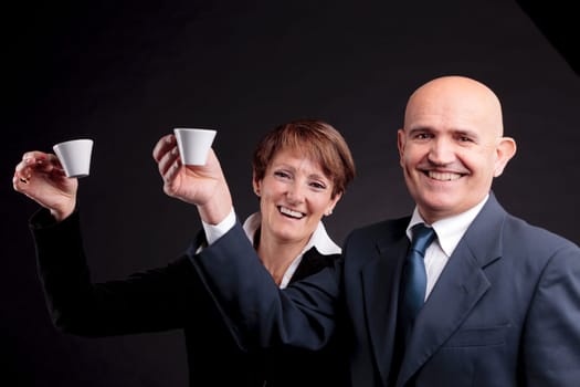 a smiling elderly couple holding up two cups of italian espreso coffee and smiling each other
