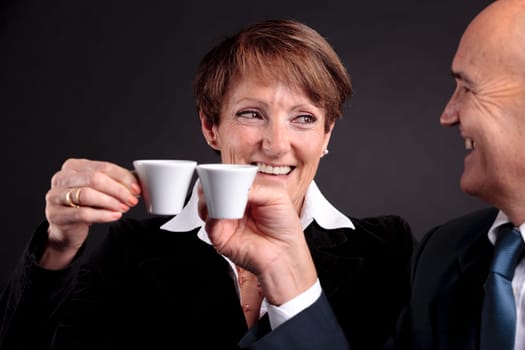 a smiling elderly couple holding up two cups of italian espreso coffee and smiling each other