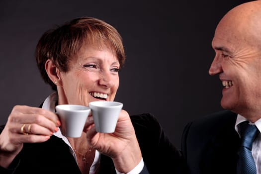 a smiling elderly couple holding up two cups of italian espreso coffee and smiling each other