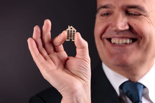 an old self confident man smiling with a little wooden house between his fingers