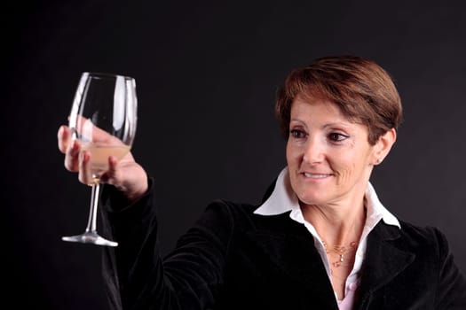 pretty old woman rising up a glass of wine and watching it (focus on the face)