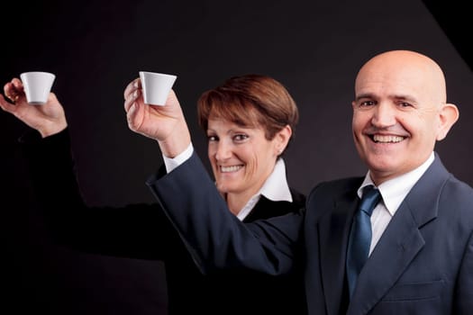a smiling elderly couple holding up two cups of italian espreso coffee and smiling each other