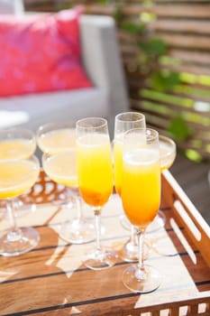 Closeup of glasses of orange juice on wooden serving tray at outdoor party in sunlight