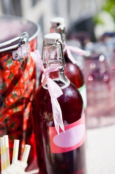 Closeup of two bottles of strawberry based fruit juice with decorative ribbons and labels on table at outdoors party in sunlight