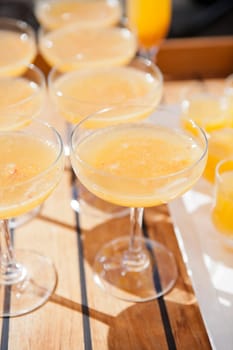 Closeup of glasses of orange juice in rows on wooden serving tray at outdoor party in sunlight
