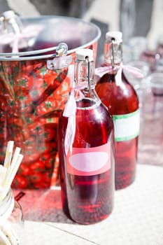 Closeup of two bottles of strawberry based fruit juice with decorative ribbons and labels on table at outdoors party in sunlight
