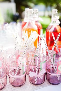 Closeup of decorative pink colored party glasses with straws on table outdoors with bottle of fruit juice in background