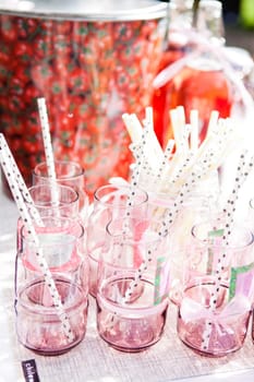 Closeup of decorative pink colored party glasses with straws on table outdoors on bright day