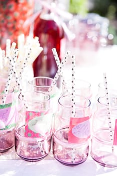 Closeup of decorative pink colored party glasses with straws on table outdoors with bottle of fruit juice in background