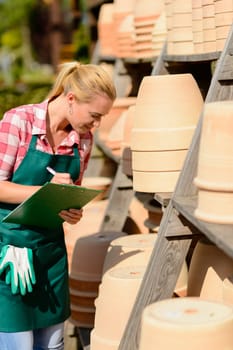 Garden center woman worker write notes by clay pots shelf