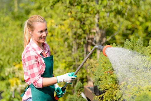 Garden center woman worker watering plants with hose smiling sunny
