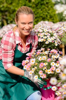Garden center woman worker holding pink potted flowers smiling sunny