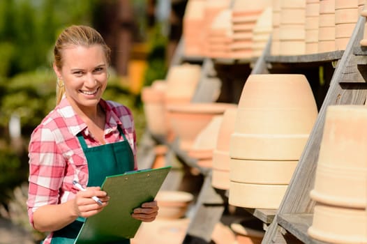 Garden center woman worker standing by clay pots shelf smiling