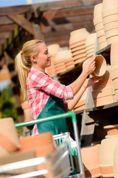 Garden center woman worker with clay pots on shopping cart