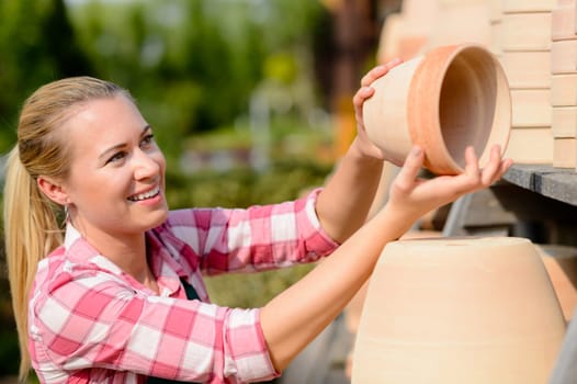 Garden center woman worker putting clay pots on shelf smiling