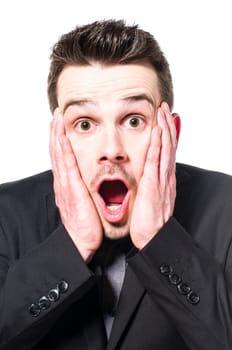 Young businessman in a suit holds both hands on the face and looking scared with open mouth at the camera.