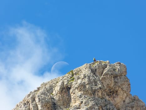 Mountaineers high up on a peak with blue sky and moon.
