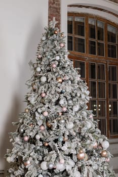 Artificial Christmas tree in a bright interior with silver flowers and snow on the branches. The concept of New year and Christmas