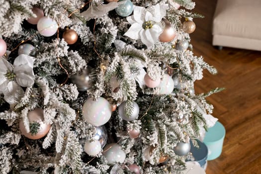 big Christmas tree in a bright interior with silver, pink, bronze balls and snow on the branches. Present boxes under tree.The concept of New year and Christmas. Luxury Christmas tree with glowing garland.