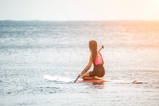 Sea woman and man on sup. Silhouette of happy young woman and man, surfing on SUP board, confident paddling through water surface. Idyllic sunset. Active lifestyle at sea or river