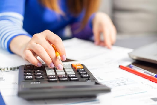 Close up young woman using calculator, managing household monthly budget, summarizing taxes or bills, planning future investments, doing financial affairs at home, accounting bookkeeping concept