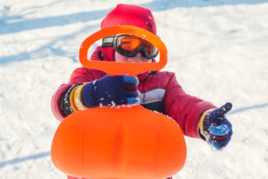 A boy is riding a sledge in snowy park in winter. Child outdoor activities.