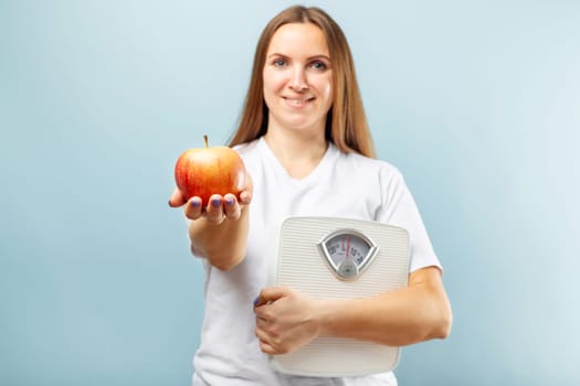 Happy smiling woman holding weight scales and red apple on a blue background. Healthy eating concept. Diet