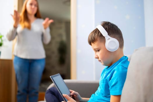 Mother scolds her son. Boy uses tablet computer with headphones and ignores his mom. Family relationships concept