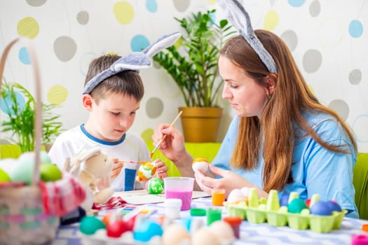 Happy Easter. A mother and her son painting Easter eggs. Happy family getting ready for Easter. Mom and child boy wearing bunny ears on Easter day