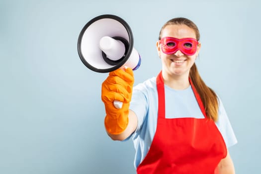 Young woman in red mask, rubber gloves and apron with megaphone on blue background with copyspace. Mockup. Advertising