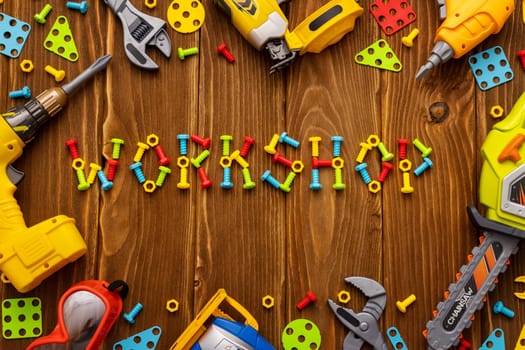 Colorful toy tools, bolts and nuts as frame with text WORKSHOP on wooden background. Top view. Flat lay