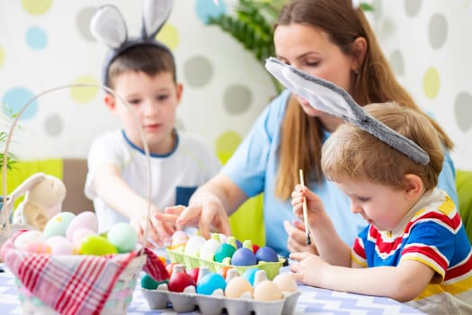 Happy Easter. A mother and her children painting Easter eggs. Happy family getting ready for Easter. Cute boys wearing bunny ears on Easter day