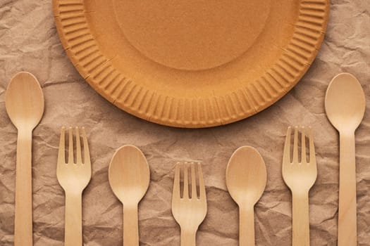 Wooden forks and spoons and paper plate on crumpled paper. Biodegradable eco-friendly dishes