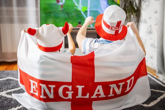 Father and son with England flag watching soccer game on TV and supporting their national football team