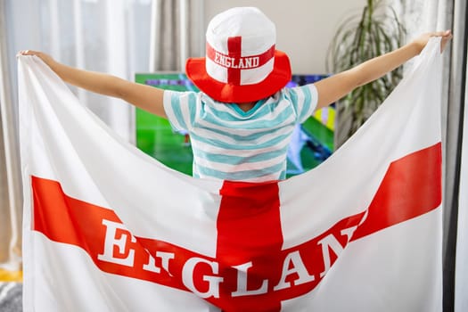 A boy with England flag watching soccer game on TV and supporting his national football team
