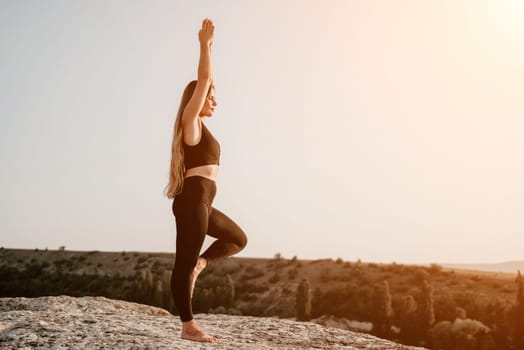 Well looking middle aged woman with long hair, fitness instructor in leggings and tops doing stretching and pilates on the rock near forest. Female fitness yoga routine concept. Healthy lifestyle.