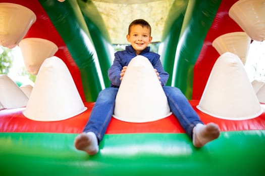 Happy kid having fun on colorful inflatable attraction playground. Child have fun and ride on the outdoor playground.