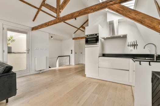 a kitchen and living room in an attic style home with wood beams on the ceiling, white walls and hardwood flooring