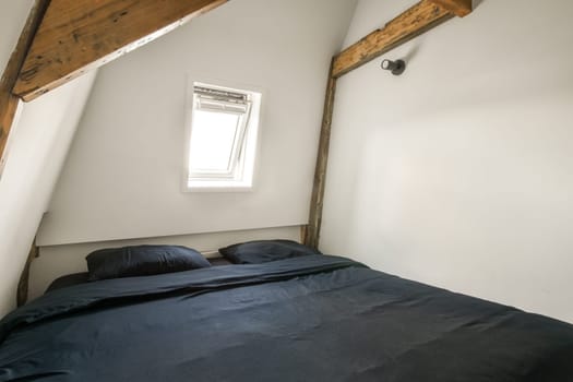 a bed in a room with white walls and wood beams on the ceiling above it is a window that looks out to the outside