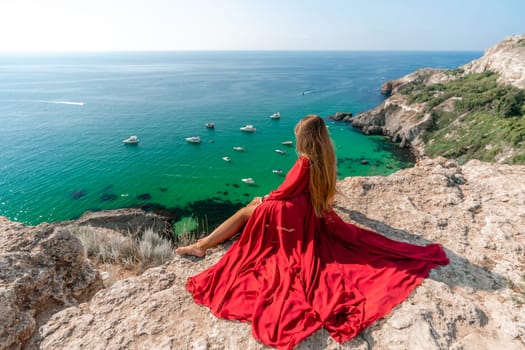 Woman red dress sea. Happy woman in a red dress and white bikini sitting on a rocky outcrop, gazing out at the sea with boats and yachts in the background