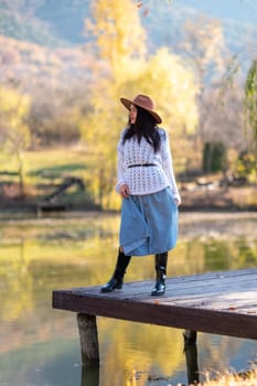 Autumn lake woman. She stands by a pond on a wooden pier in autumn and admires nature. The concept of tourism, weekends outside the city