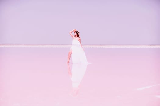 Woman in pink salt lake. She in a white dress and hat enjoys the scenic view of a pink salt lake as she walks along the white, salty shore, creating a lasting memory