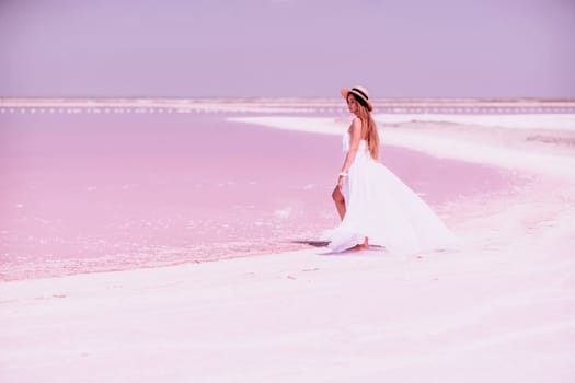 Woman in pink salt lake. She in a white dress and hat enjoys the scenic view of a pink salt lake as she walks along the white, salty shore, creating a lasting memory