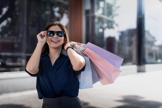 Happy beautiful young stylish woman asian with shopping bag while walking near mall on holiday Black Friday.