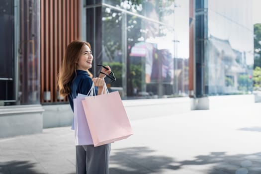 Happy beautiful young stylish woman asian with shopping bag while walking near mall on holiday Black Friday.