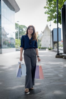 Happy beautiful young stylish woman asian with shopping bag while walking near mall on holiday Black Friday.